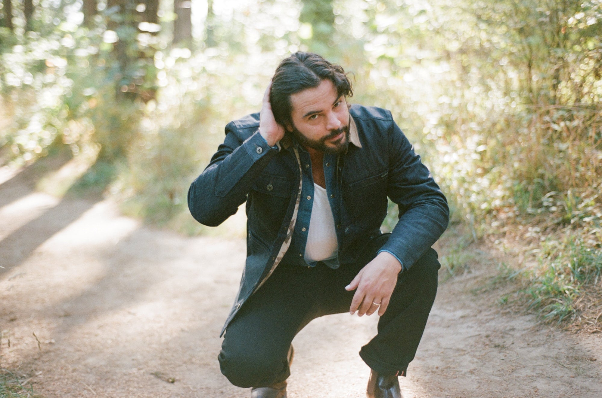 Man wearing a Native American Ginew lined denim chore coat on a dirt path in a forest